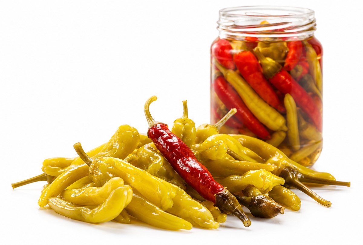 Pickled yellow and red peppers beside a filled jar